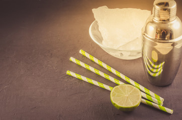 Cocktail shaker, lime, ice and straws/Cocktail shaker, lime, ice and straws on a dark background. Selective focus and copyspace