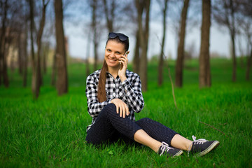 Young attractive woman sitting on grass and talk by phone relaxing resting in sunny weather in field on bright green background. Lifestyle, leisure concept