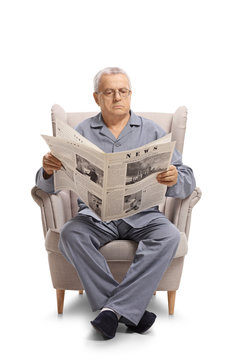 Mature man in pajamas sitting in an armchair and reading a newspaper