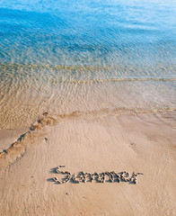 The word summer is written in the sand. The inscription is made by hand. Blue sea wave.