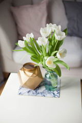 Interior. Room. A bouquet of tulips in a glass vase, a gold candlestick on a white wooden table. Sofa, pillows. Spring. It's cozy. Living room.