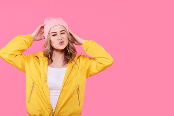 Crazy beautiful trendy girl in bright yellow jacket and pink beanie hat puckering lips. Attractive...