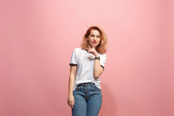 The young woman whispering a secret behind her hand over pink background