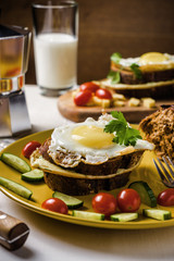 Dish of sandwich with fried eggs, cucumbers and cherry-tomatoes with bread and milk on linen tablecloth, dark and moody.