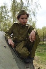 Boy in the military uniform on the tank of time of Second World War. Kids in uniform. Soldier boy. War time.