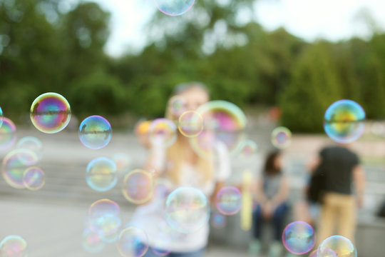 Blurred background with shallow depth of field. The girl lets the soap bubbles in the park, has a fun weekend.