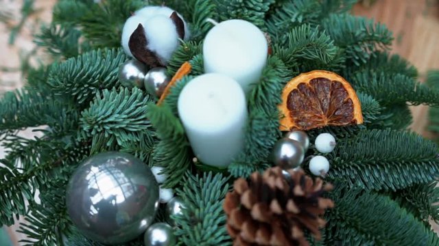 Christmas composition: pine tree branches, candles, christmas tree toys, pinecones, artificial berries, dry orange slices and cotton flower balls on wooden table, close-up. Holiday spirit atmosphere.