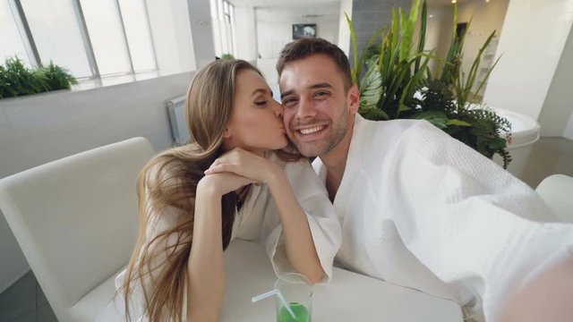 Point of view shot of attractive loving couple recording video while relaxing in day spa together. Young people are smiling, laughing and kissing looking at camera.