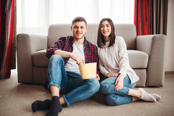 Couple sitting on floor and watch tv with popcorn