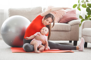 Young pretty mother working out with her little child at home