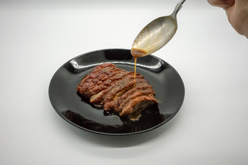 Woman hand holding silver spoon adding sauce on top of roasted duck