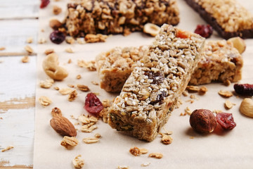 Various granola chocolate energy bars in row with scattered mixed nuts, cereals & dried fruit, grunged white wood table background. Healthy vegan fitness food snack. Top view, copy space, close up.
