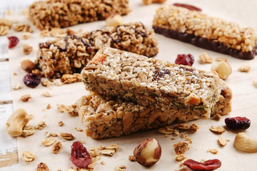 Various granola chocolate energy bars in row with scattered mixed nuts, cereals & dried fruit, grunged white wood table background. Healthy vegan fitness food snack. Top view, copy space, close up.