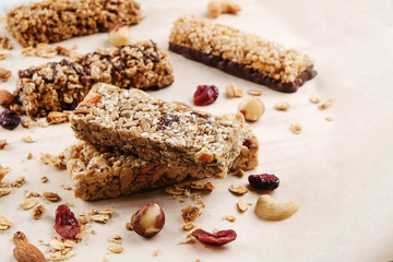Various granola chocolate energy bars in row with scattered mixed nuts, cereals & dried fruit, grunged white wood table background. Healthy vegan fitness food snack. Top view, copy space, close up.