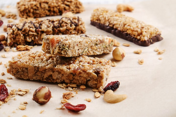 Various granola chocolate energy bars in row with scattered mixed nuts, cereals & dried fruit, grunged white wood table background. Healthy vegan fitness food snack. Top view, copy space, close up.