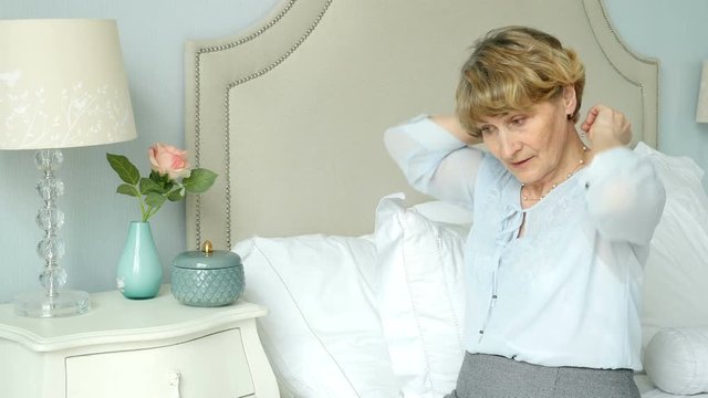 Elderly woman sits in the bedroom and takes off jewelry