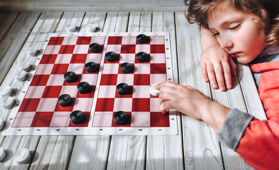 The funny sad caucasian child plays checkers. Children's hand on a checkerboard. Play board games....