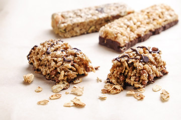 Various granola chocolate energy bars in row with scattered mixed nuts, cereals & dried fruit, white wood table background. Healthy vegan fitness food, dietary snack. Top view, copy space, close up.
