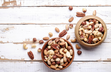 Mixed nuts in wooden bowl and scattered on table. Trail mix of pecan, almond, macadamia & brazil edible nuts with walnut hazelnut on wood textured surface. Background, copy space, top view, close up.