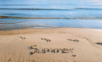 The word summer is written in the sand. Blue sea wave. Summer beach concept.