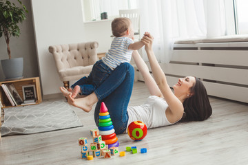 Young pretty mother playing with her little son. Cheerful family having fun indoors with little...
