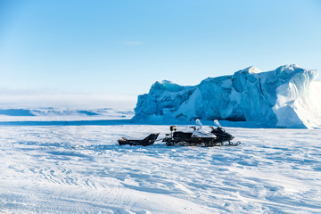 Near the iceberg on the snow, two snowmobiles. The landscape in the Arctic. The Arctic ocean.