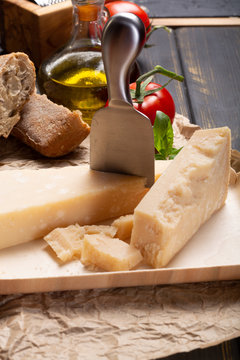 Traditional italian food - aged Italian parmesan hard cheese Parmigiano-Reggiano with cheese knife, tomato, basil, olive oil