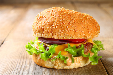 Tasty homemade burger consisting of bun, patties, salad, red onion and tomato on an old wooden table.