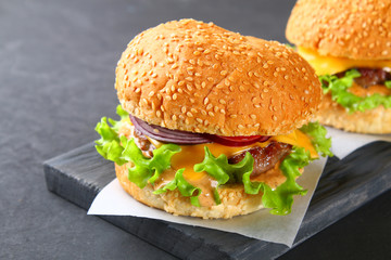 Tasty homemade burger consisting of bun, patties, salad, red onion and tomato on a dark black concrete background, table.