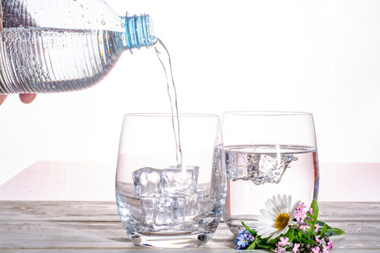 Pouring of sparkling soda mineral drink water in glasses with ice cubes close up copy space
