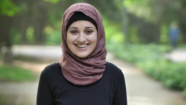 Portrait of a young smiling girl in a hijab, on nature, in a park in the background. 50 fps