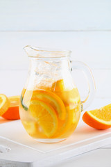 Orange detox water in a jug on a white wooden table. Healthy food, drinks.