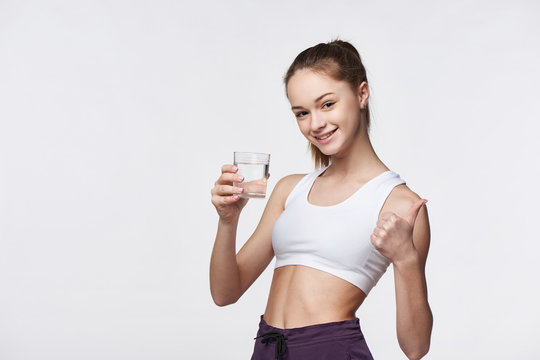 Sporty teen girl with glass of water in hand gesturing thumb up