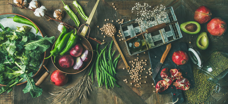 Winter vegetarian, vegan food cooking ingredients. Flat-lay of seasonal vegetables, fruits, beans, cereals, kitchen utencils, dried flowers, olive oil over wooden background, top view. Healthy food