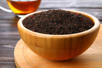 Black dry tea with a cherry in a bowl on a wooden table.