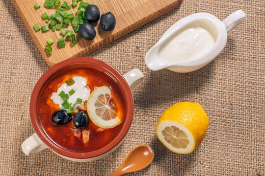 Soup saltwort with meat, potatoes, tomatoes, lemon, black olives and sour cream in ceramic soup bowl