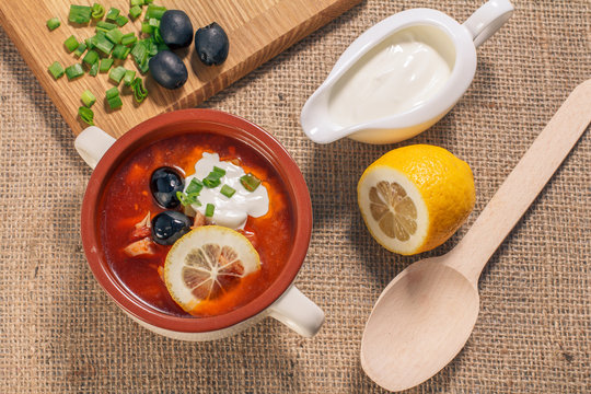 Soup saltwort with meat, potatoes, tomatoes, lemon, black olives and sour cream in ceramic soup bowl