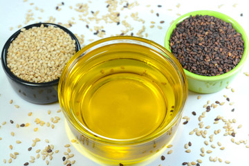 Sesame oil in a glass cup with sesame black and white seeds in a cup.