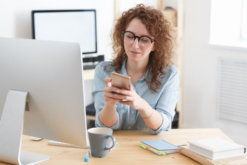 Obraz premium Zadowolona kobieta z radosnym wyrazem twarzy udostępnia zdjęcia w sieciach społecznościowych, siedząc przed cyfrowym komputerem w miejscu pracy w kreatywnym studio. Mała przerwa w ciężkim dniu pracy