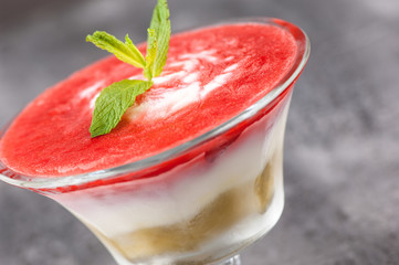 fruit smoothie with a petal in a glass vase on a gray surface.