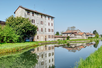 Obraz premium Buildings on a limpid mirrored river in a sunny day, in Certosa of Pavia, Italy. HDR effect.