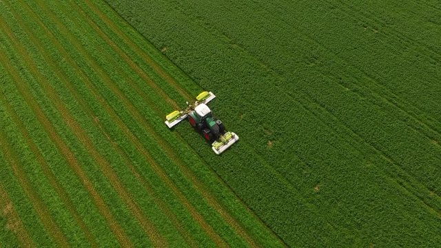 Aerial view of a tractor mowing a green fresh grass field, 
a farmer in a modern tractor mowing a green fresh grass field on a sunny day.