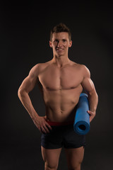 Fototapeta na wymiar Sportsman smile with sexy torso and six pack. Happy man hold yoga mat. Athlete smiling with strong arms in shorts. Gym equipment for training and workout. Sport yoga and fitness activity