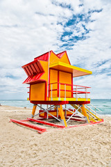 Fototapeta premium Lifeguard house on sand beach in miami, usa. Tower for rescue baywatch in typical art deco style. Wooden house on ocean shore on cloudy sky. Summer vacation concept. Public guarding and safety