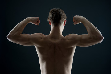 Fototapeta na wymiar Athlete with fit torso, back view. Man bodybuilder flex arm muscles. Sportsman show biceps and triceps. Workout and training activity in gym. Power and strength concept