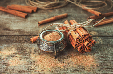 Ground cinnamon, cinnamon sticks, tied with jute rope on old wooden background in rustic style