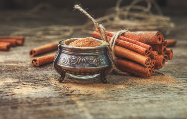 Ground cinnamon, cinnamon sticks, tied with jute rope on old wooden background in rustic style