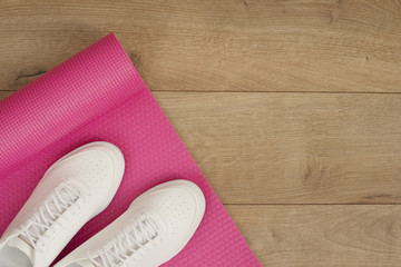 Pink yoga mat and white trendy sneakers on a wooden background. Fitness concept, active lifestyle, body care concept. Wood Background