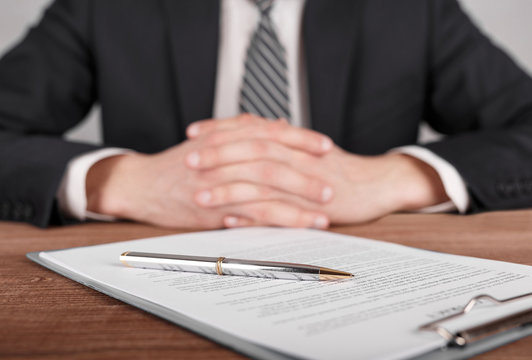 Man in suit is sitting in front of contract with crossed arms.