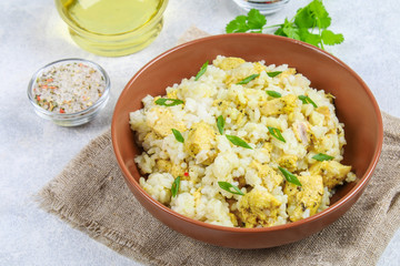 White steamed rice with slices of fried chicken fillet in a bowl on a concrete table.